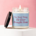 Lit candle in glass jar with blue label text "The Best Thing He Ever Brought Home"