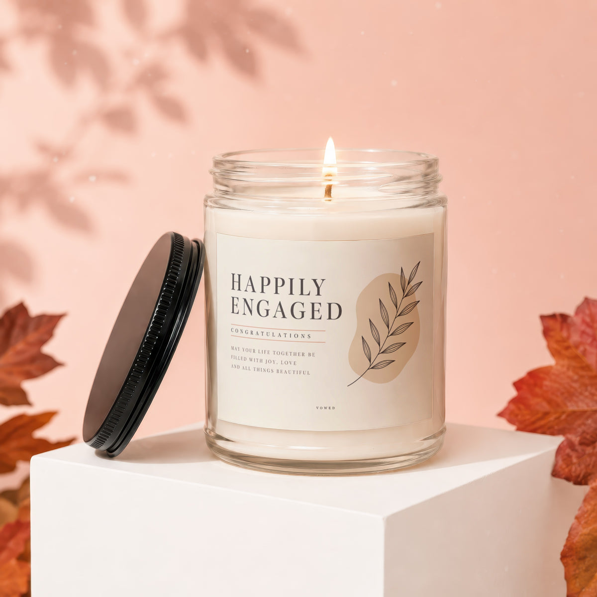 Candle with "Happily Engaged" text and floral design, lid off.
