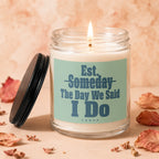 Glass candle with lit wick and teal label reading "Est. Someday The Day We Said I Do Vowed".