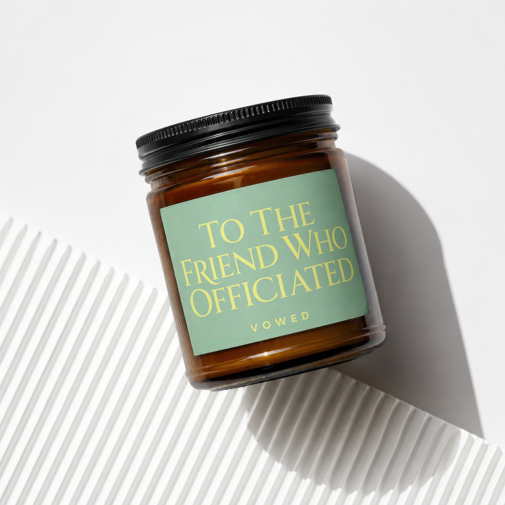 Amber glass candle with a light green label that reads "TO THE FRIEND WHO OFFICIATED VOWED".
