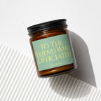Amber glass candle with a light green label that reads "TO THE FRIEND WHO OFFICIATED VOWED".