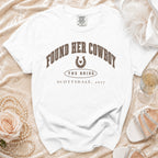 White t-shirt with brown text reading Found Her Cowboy, The Bride, Scottsdale, 2027, and a horseshoe graphic.