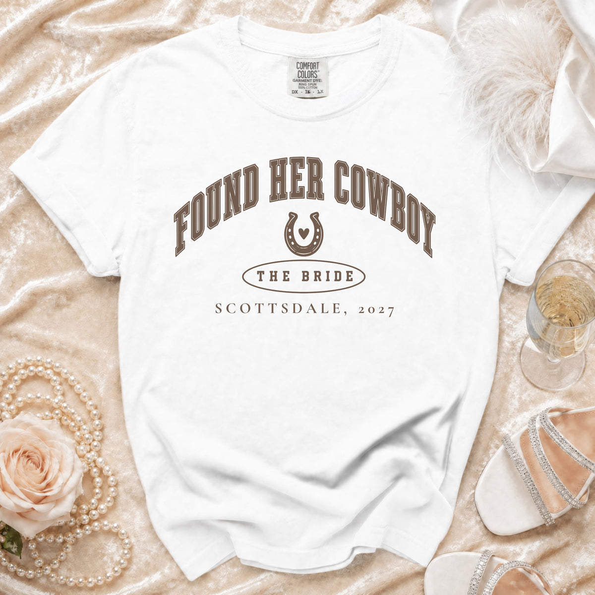 White t-shirt with brown text reading Found Her Cowboy, The Bride, Scottsdale, 2027, and a horseshoe graphic.