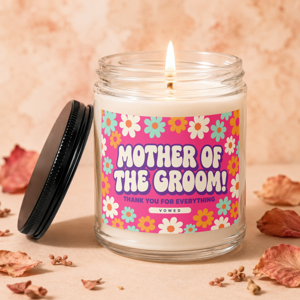 Glass candle with lit wick, featuring a "Mother of the Groom" label with flowers.