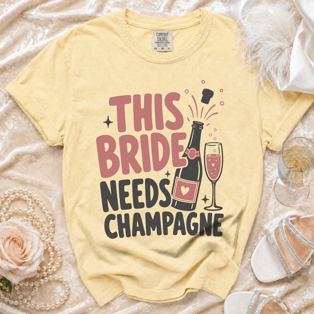 Yellow t-shirt with "This Bride Needs Champagne" text, champagne bottle and glass.