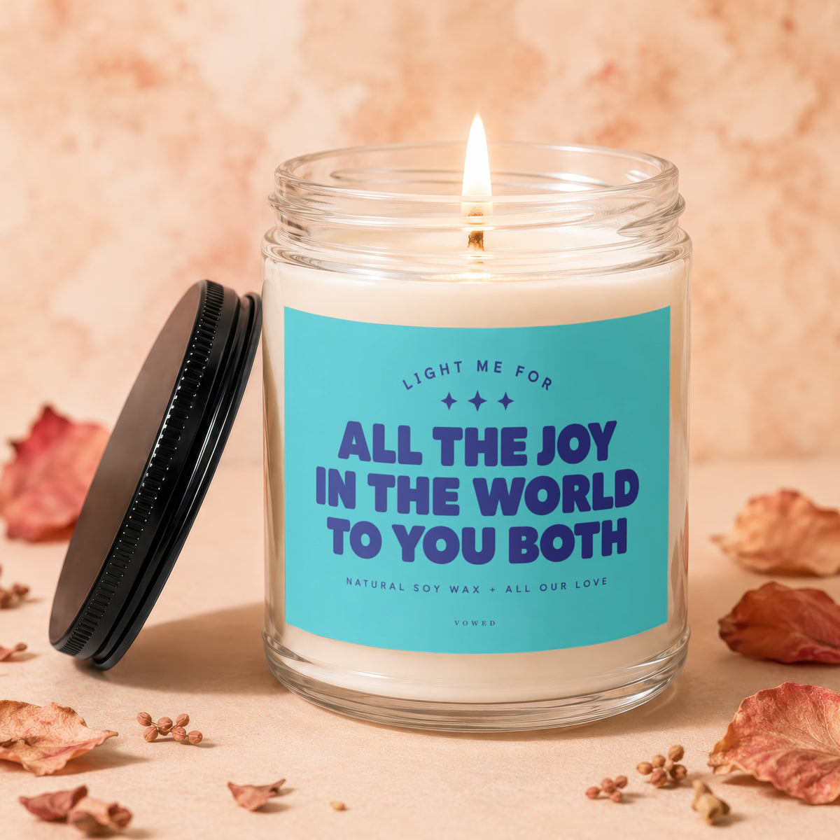 Glass candle with lit wick, featuring text "All the joy in the world to you both".