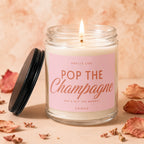 Glass jar candle with pink label reading "Smells Like Pop The Champagne She's Off The Market Vowed."