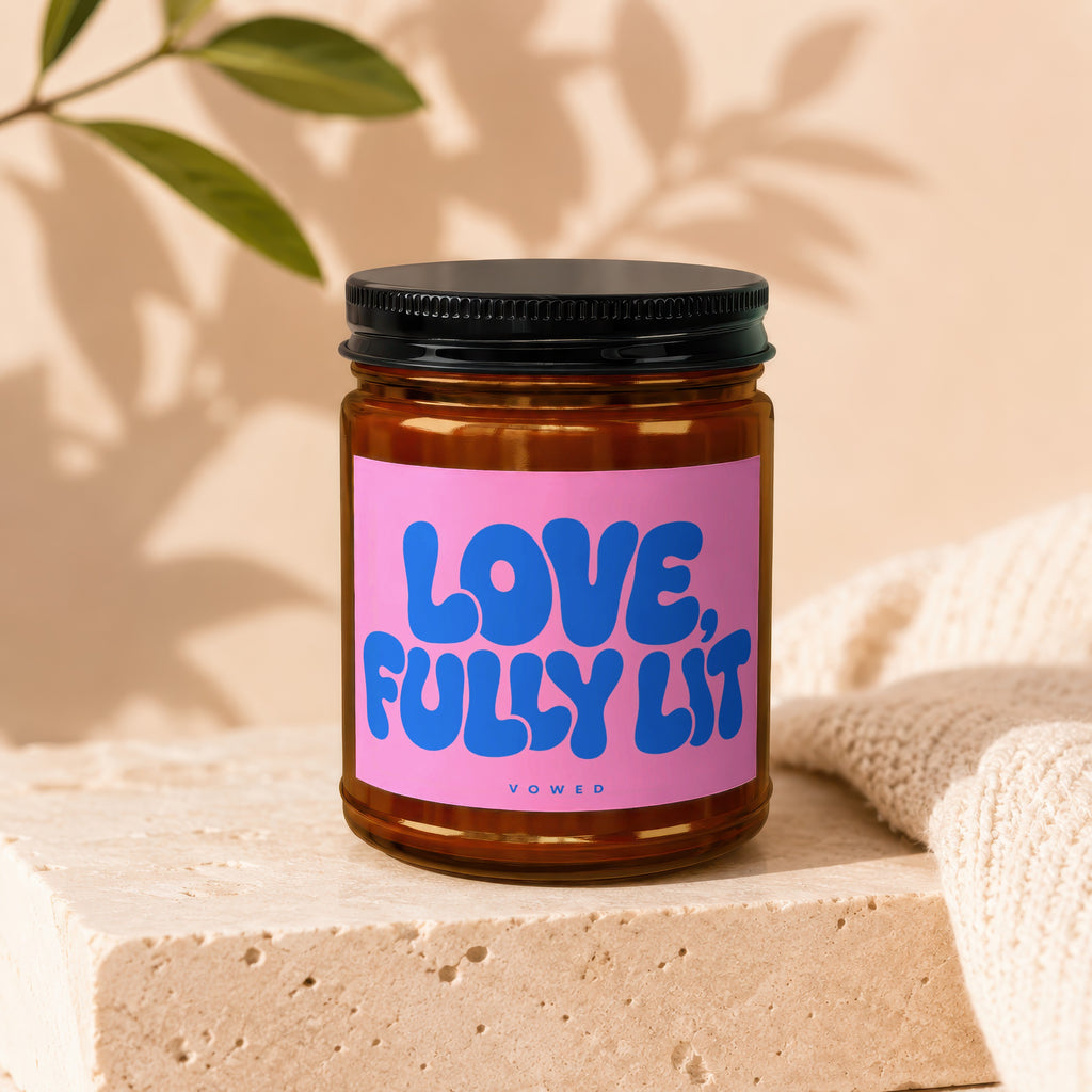 Amber jar candle with pink label reading "LOVE, FULLY LIT" and "VOWED".