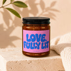 Amber jar candle with pink label reading "LOVE, FULLY LIT" and "VOWED".