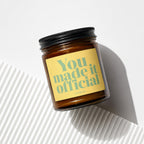 Amber jar candle with yellow label reading "You made it official"