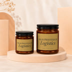 Two amber glass candles with black lids and gold labels reading "High Priestess of Logistics".