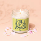 Lit white candle in glass jar with green label reading "DOUBLE PROPOSAL ENERGY VOWED".