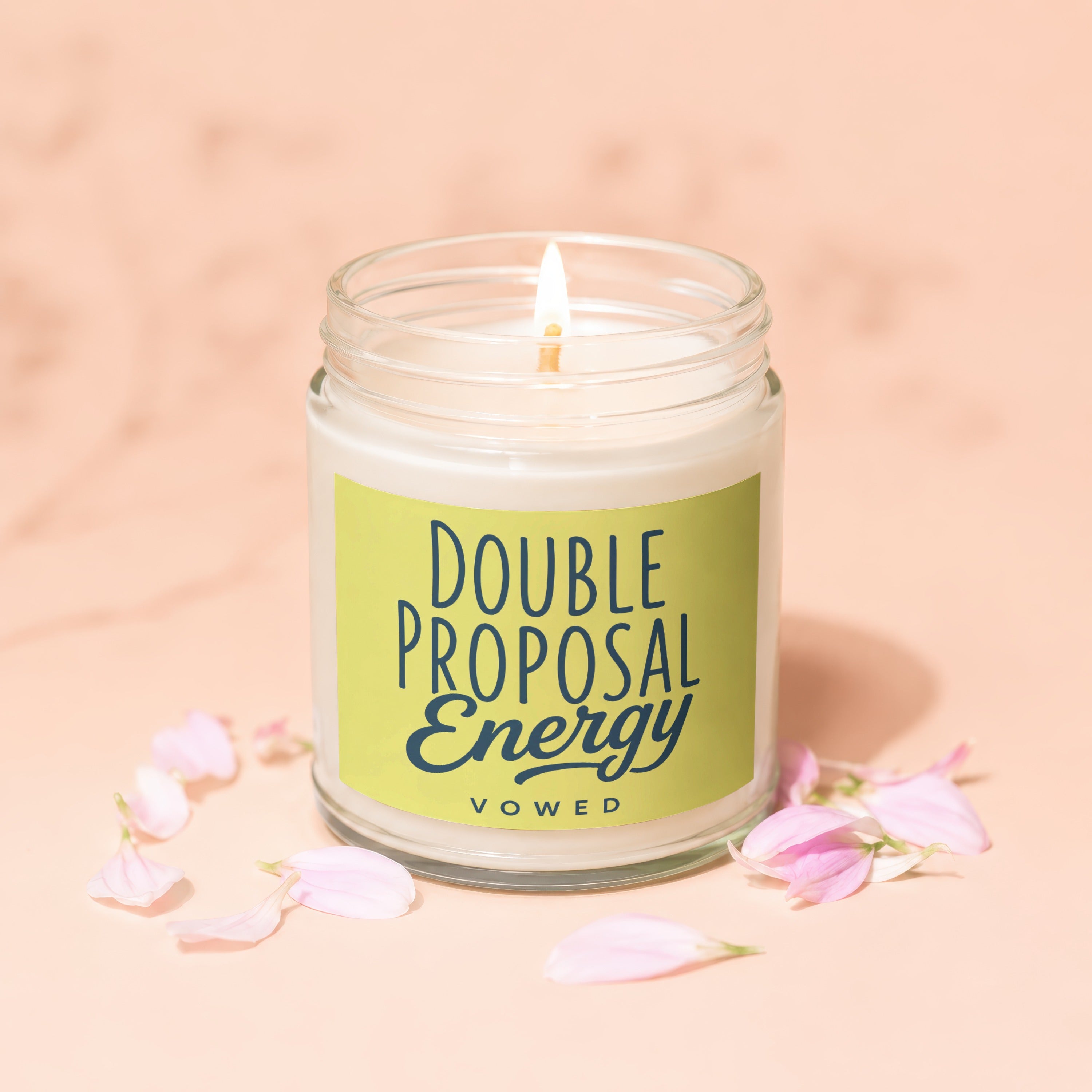 Lit white candle in glass jar with green label reading "DOUBLE PROPOSAL ENERGY VOWED".
