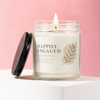 Candle with "Happily Engaged" text and floral design on a pink background.