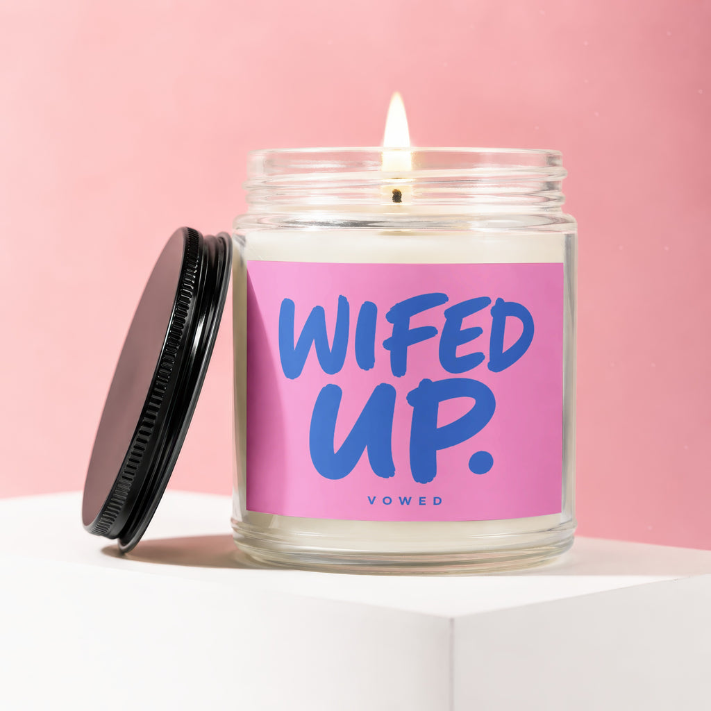 Glass candle with a lit wick, labeled "WIFED UP. VOWED" on a pink background.