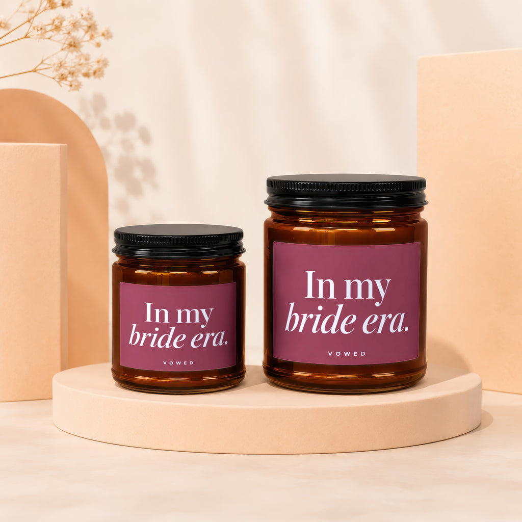 Two amber glass candles with black lids and maroon labels reading "In my bride era."