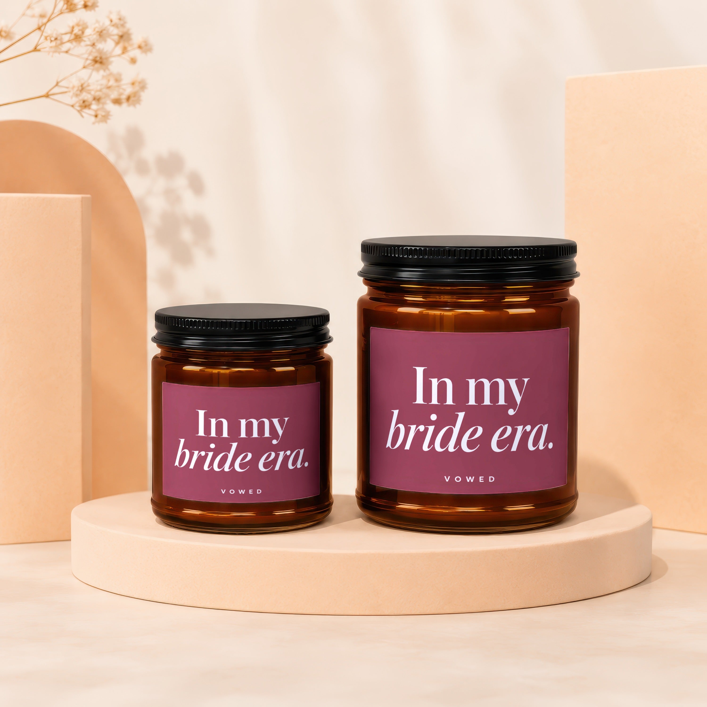 Two amber glass candles with black lids and maroon labels reading "In my bride era."