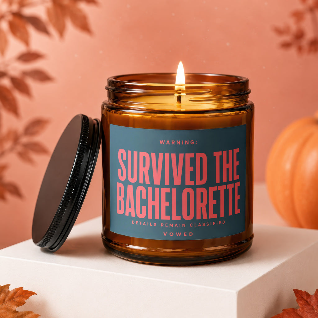 Amber jar candle with lit wick, black lid, and label that reads "Survived The Bachelorette".