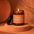 Amber glass candle with lit flame, orange label reads "I'm Fine. Everything's Fine."