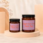 Two amber glass candles with black lids and lavender labels reading "Happily Ever After Starts Now."