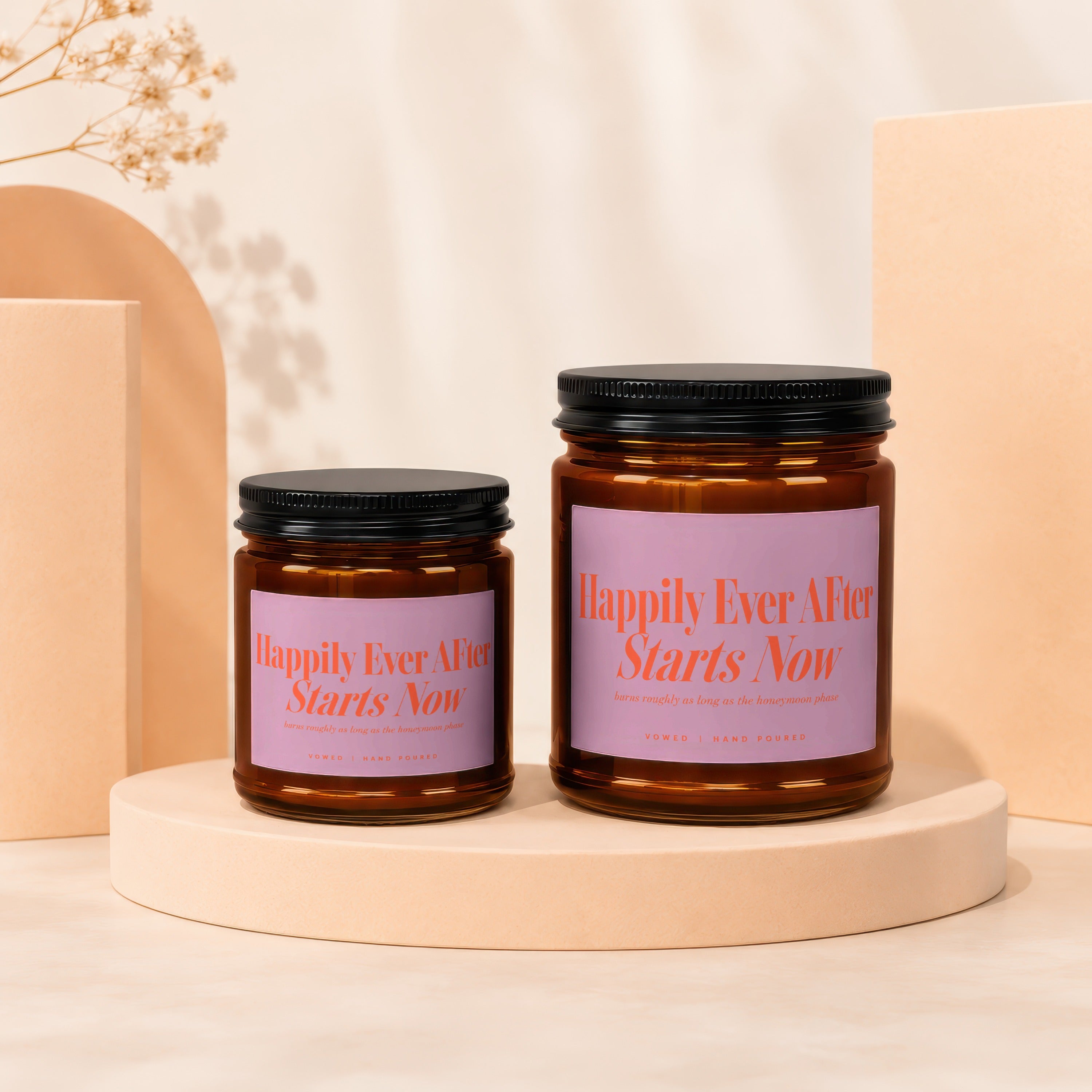Two amber glass candles with black lids and lavender labels reading "Happily Ever After Starts Now."