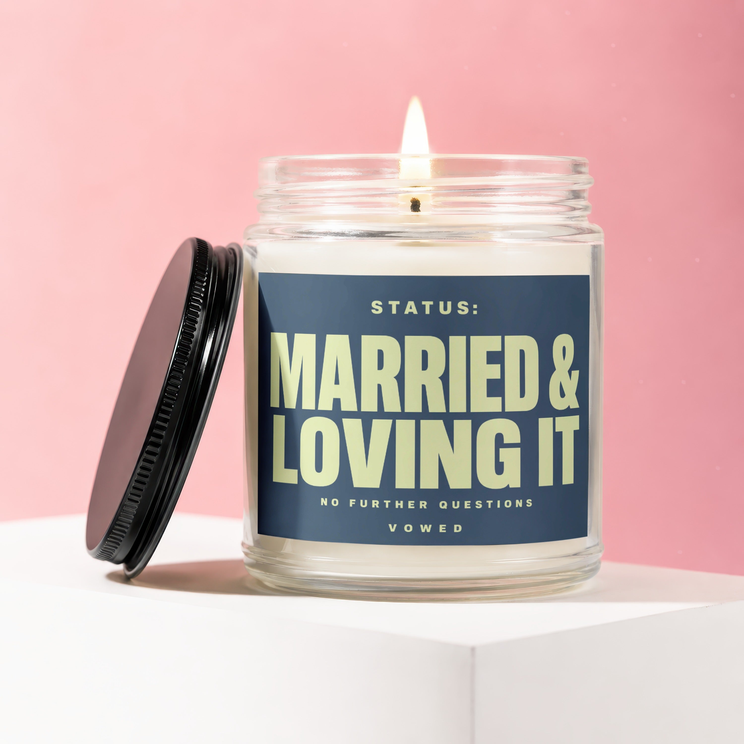 Glass jar candle labeled "STATUS: MARRIED & LOVING IT NO FURTHER QUESTIONS VOWED" on a white block.