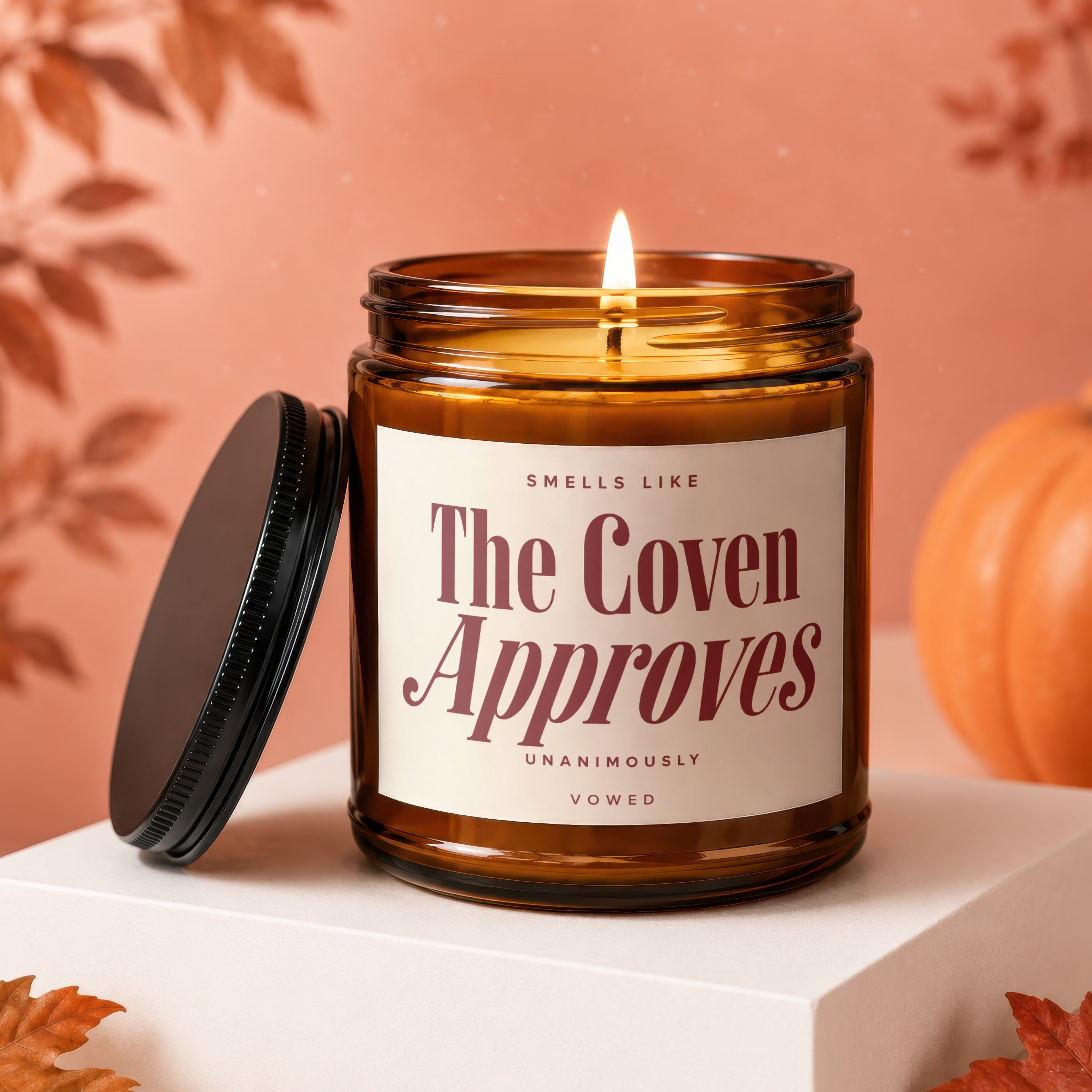 Burning amber glass candle with "The Coven Approves" label, lid to the side.