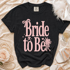 Black 'Bride to Be' t-shirt with pink text, ring, and floral accents.