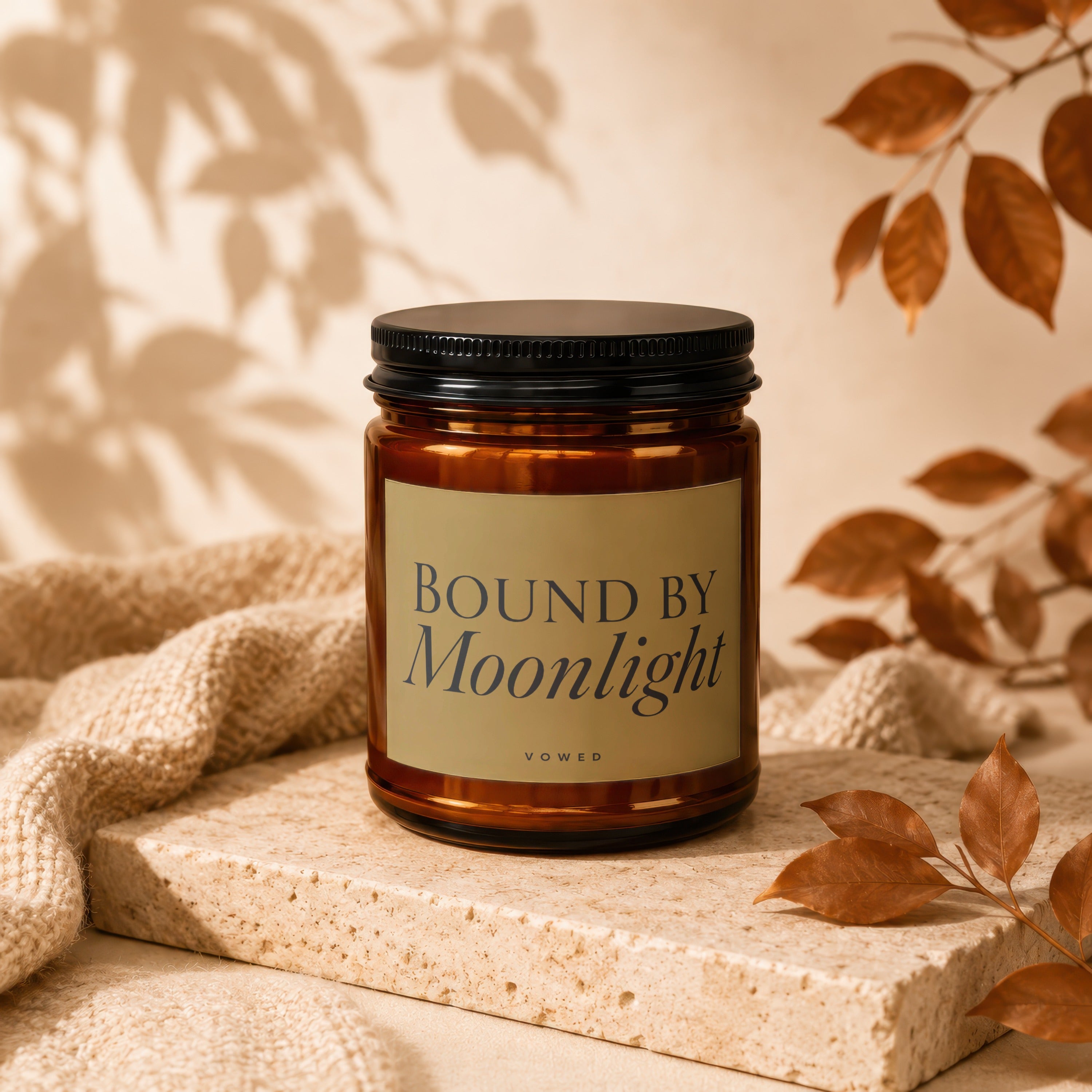Amber candle with black lid, "Bound by Moonlight" label, on a beige textured surface.