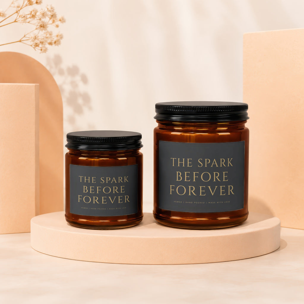 Two amber glass candles with black lids, labeled "The Spark Before Forever."