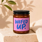 Brown glass candle in jar with pink label reading "WIFED UP." and "VOWED."