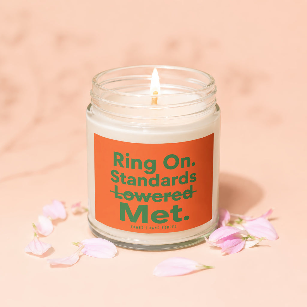 Lit candle with orange label reading "Ring On. Standards Lowered Met."