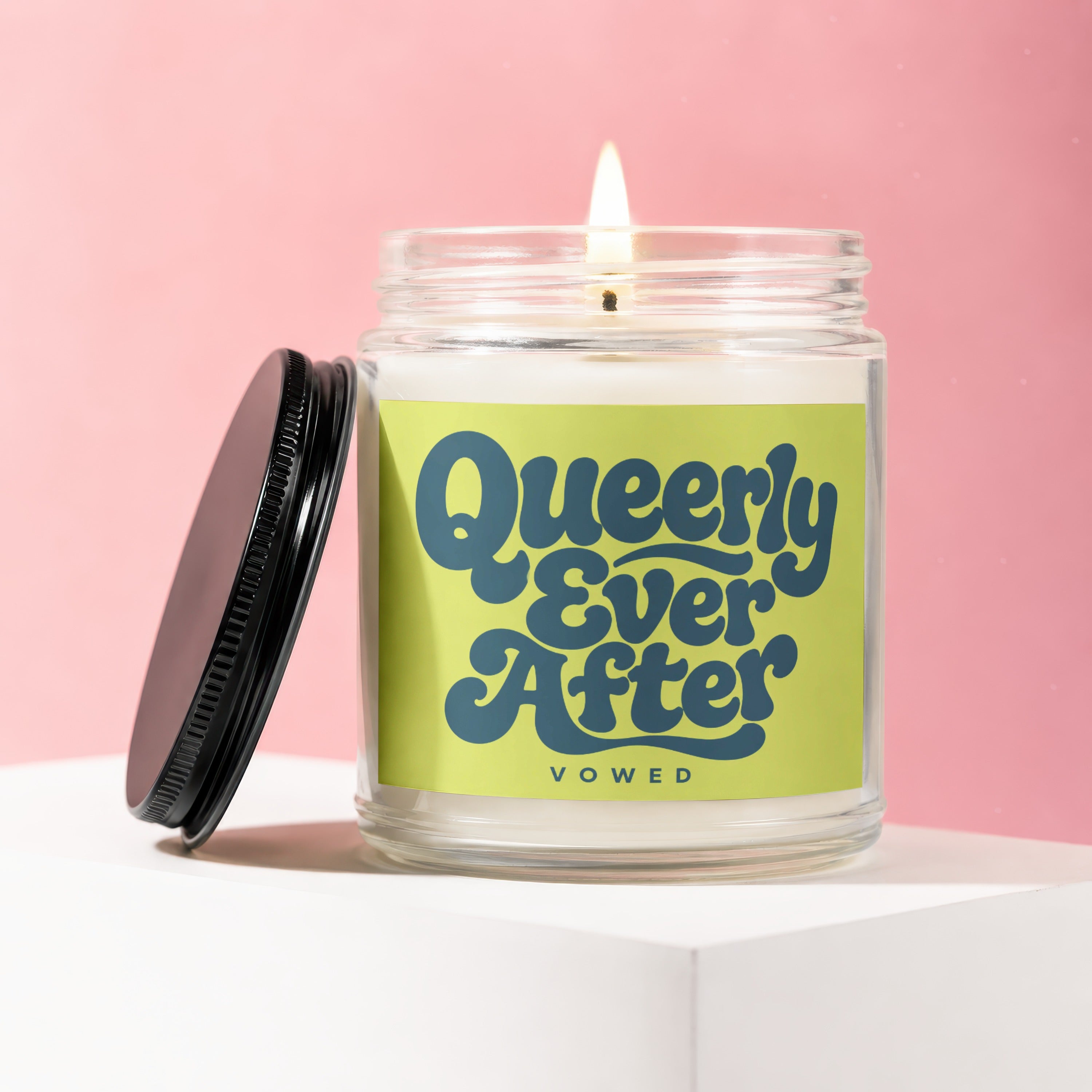 Jar candle with lit wick and black lid, labeled "Queerly Ever After Vowed".