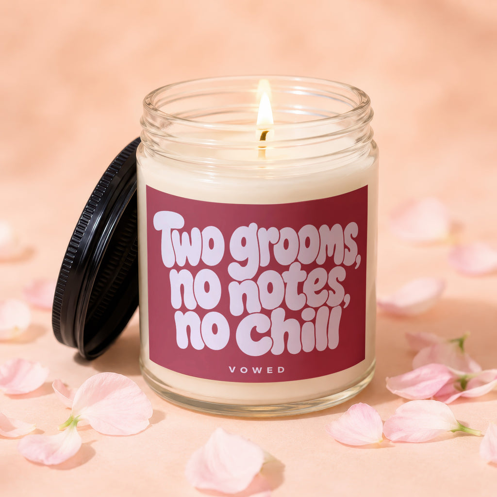 Candle with lit wick and pink label reading "Two grooms, no notes, no chill"
