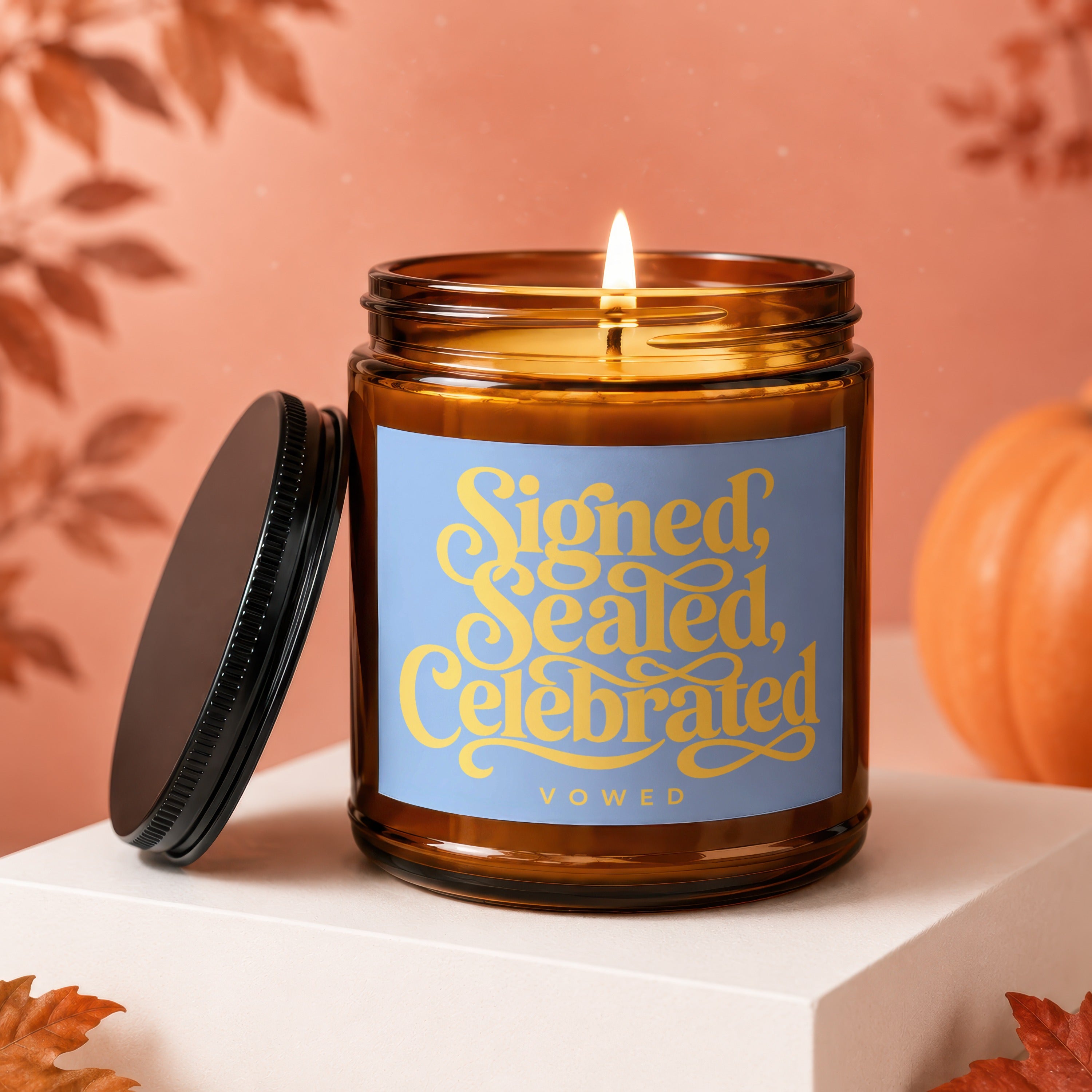 Amber candle with a lit flame and "Signed, Sealed, Celebrated VOWED" text on label.