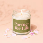 Candle with green label reading "Partner for Life VOWED" surrounded by pink petals.