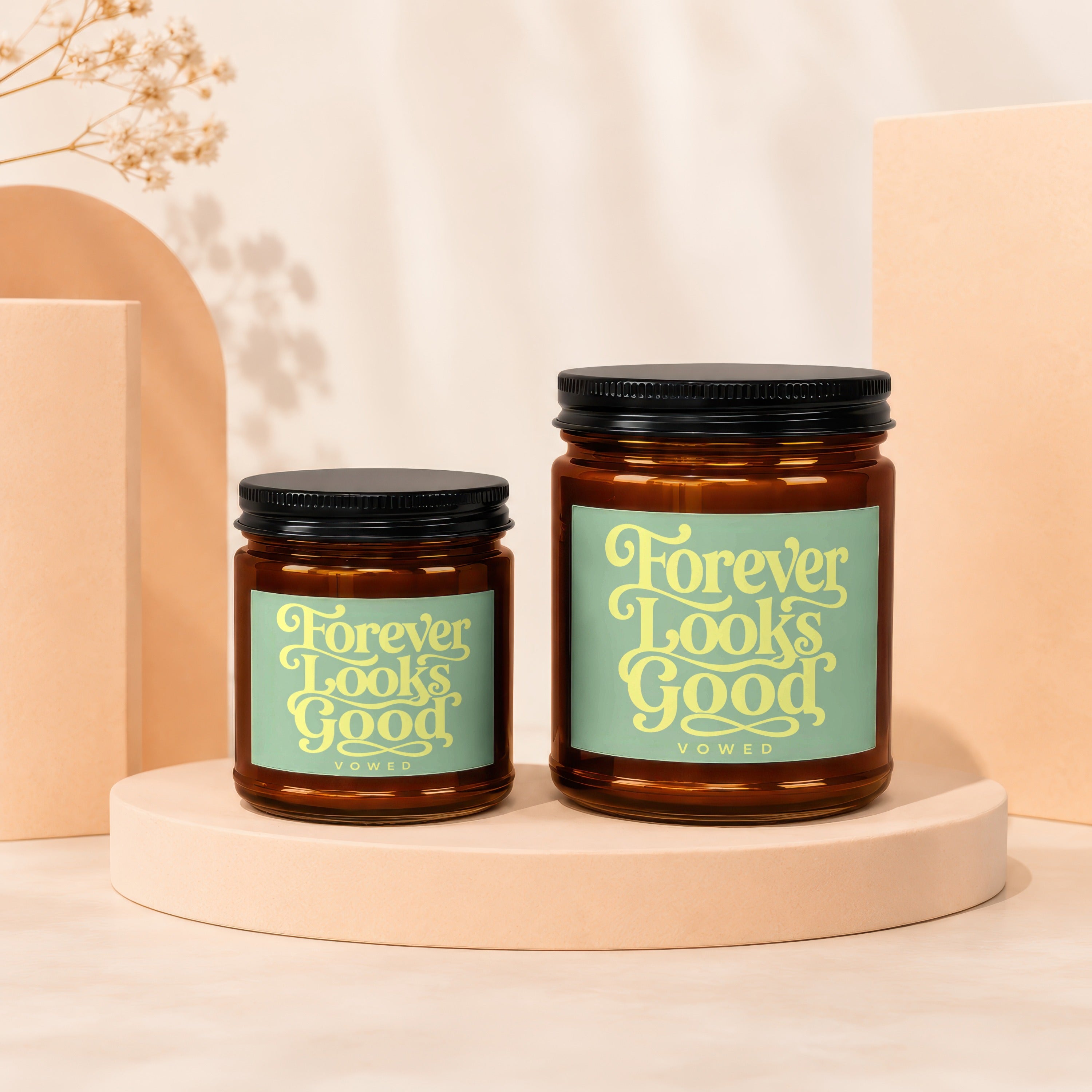 Two amber glass candles with black lids and light green labels that read "Forever Looks Good"