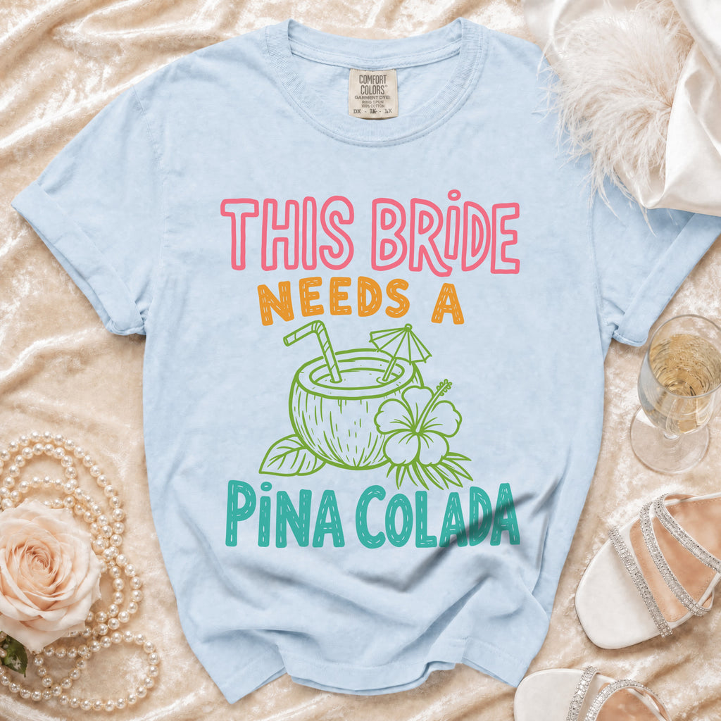 Light blue t-shirt with "THIS BRIDE NEEDS A PIÑA COLADA" text.