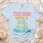 Light blue t-shirt with "THIS BRIDE NEEDS A PIÑA COLADA" text.