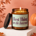 Amber glass candle with lit wick and lid beside it, stating "Best Thing on the Internet".