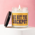 Candle with yellow label reading "Smells Like He Hit The Jackpot" on pink background.