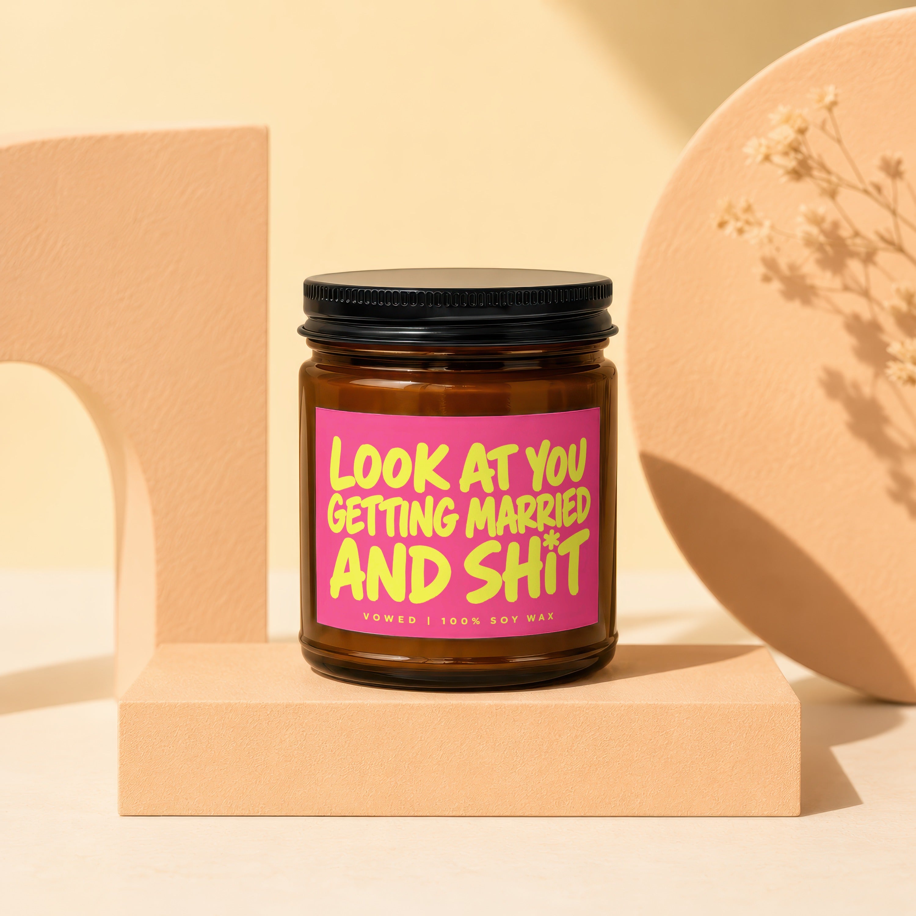 Amber jar candle with pink label that reads "Look at you getting married and shit".