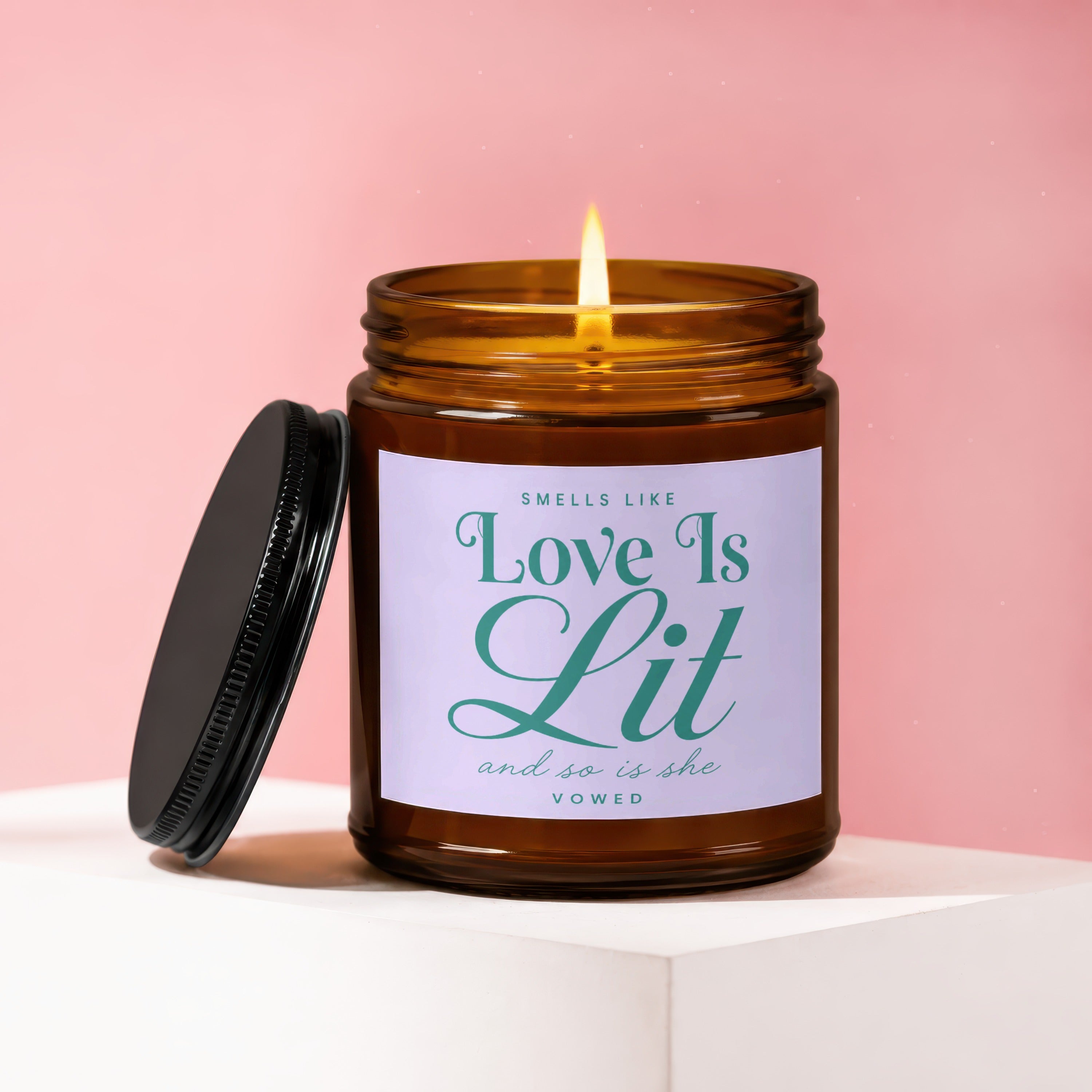 Amber glass candle with lit flame and lid, reads "Smells Like Love Is Lit and so is she vowed."