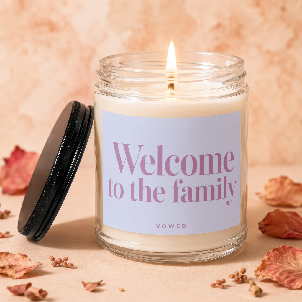 Candle with lit wick and "Welcome to the family" text on label.