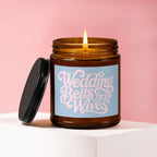 Amber candle with lit wick and black lid, labeled "Wedding Bells for the Wives".