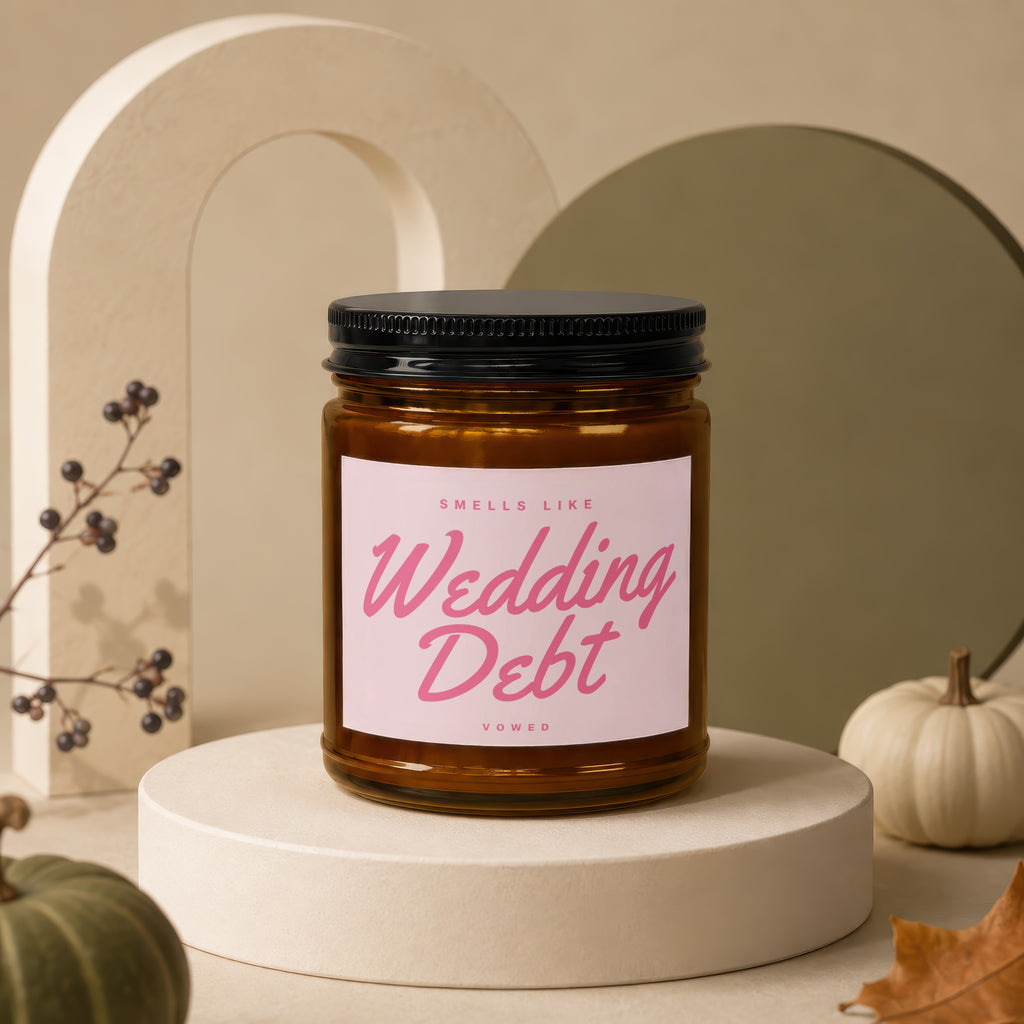 Amber jar candle with pink label that reads "Smells Like Wedding Debt" and "Vowed".