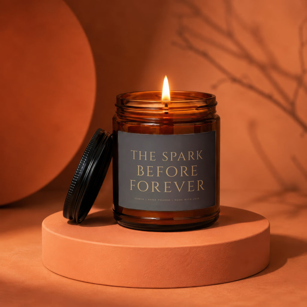 Amber glass candle with lit flame, lid off, labeled "THE SPARK BEFORE FOREVER".