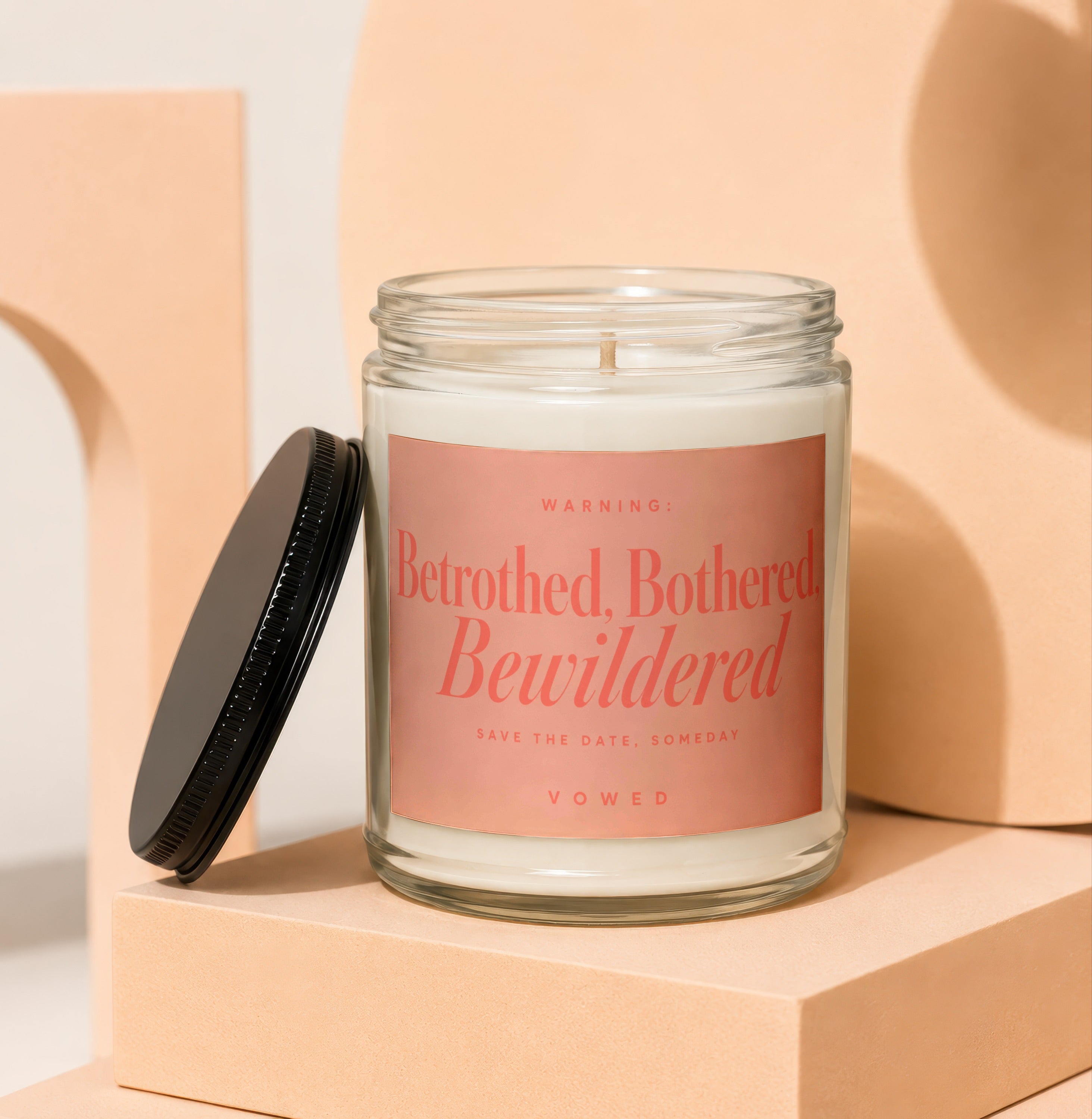 Glass candle with "Betrothed, Bothered, Bewildered" and "Vowed" text on label.