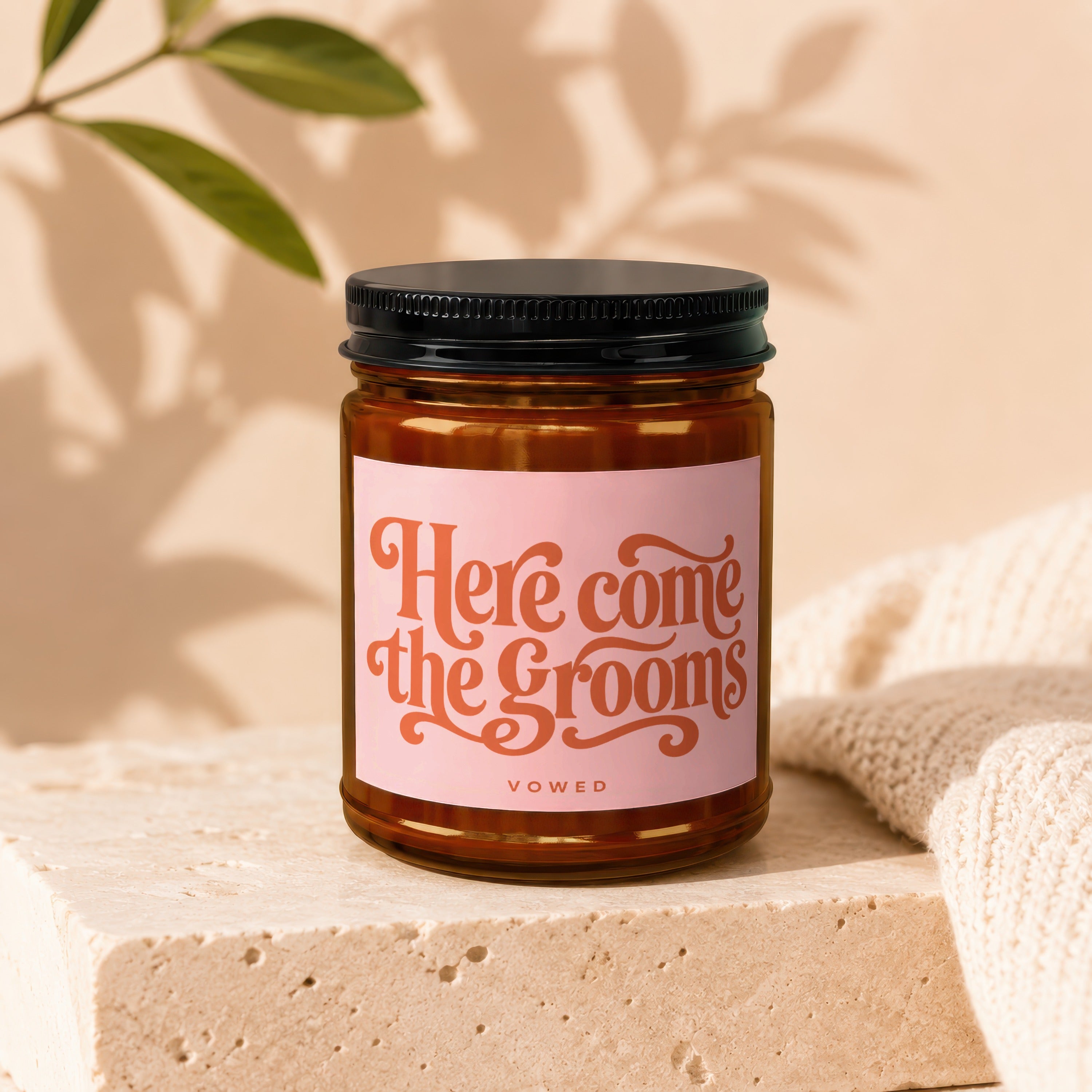 Amber candle with black lid and pink label reading "Here Come the Grooms VOWED".