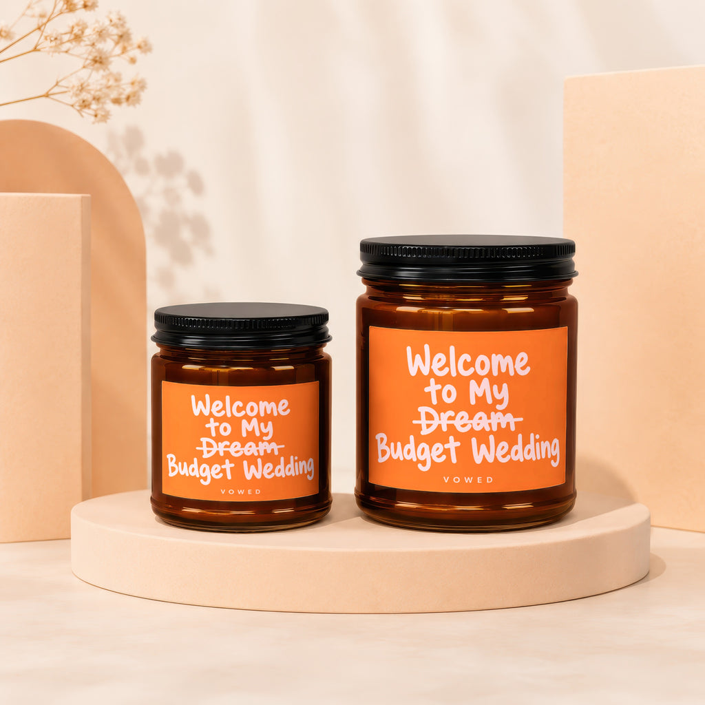Two amber candles with black lids and orange labels that read "Welcome to My Dream Budget Wedding."